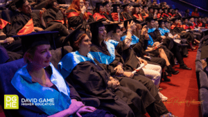 The picture shows a group of students on their graduation day. They are all sitting in the audience, dressed in gowns. If you are in the blog section, click here to read more about this article.