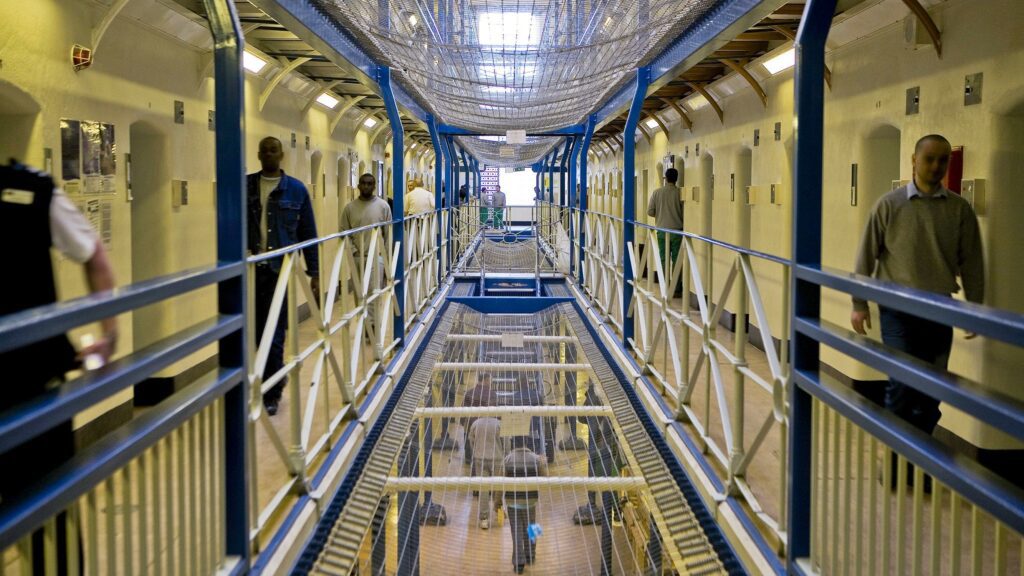 Inside the HM Prison Wandsworth Volunteer Experience. In the picture you can see the corridors of the prison, a few officers and two inmates.